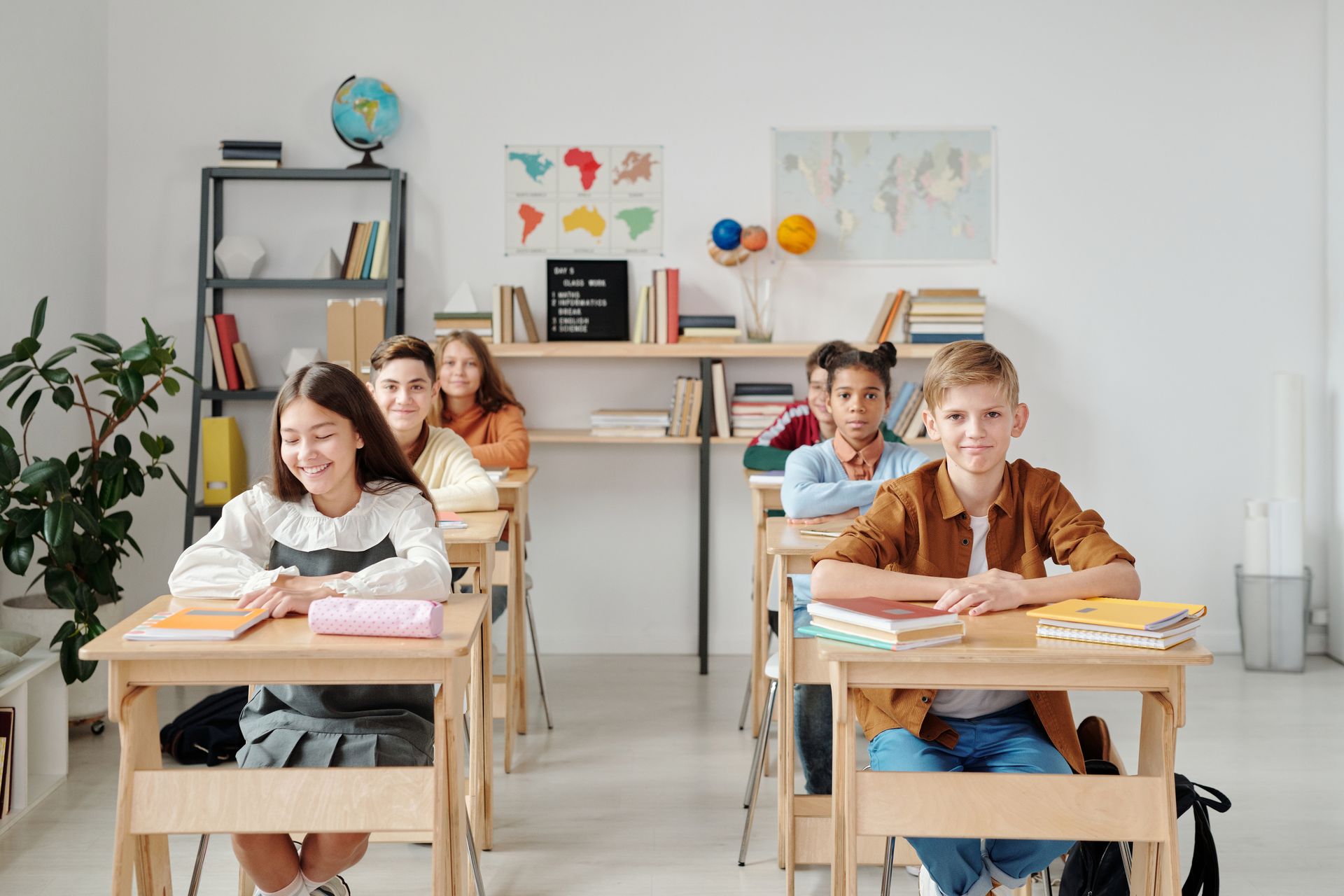 明亮的教室里摆着地球仪和世界地图,学生们坐在课桌前微笑